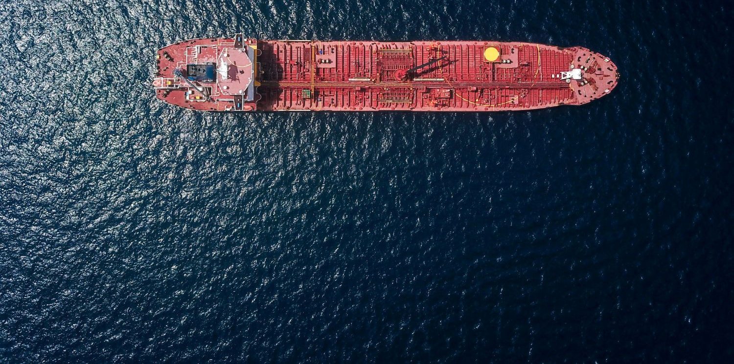 Aerial view of a red tanker underway on dark blue open water.