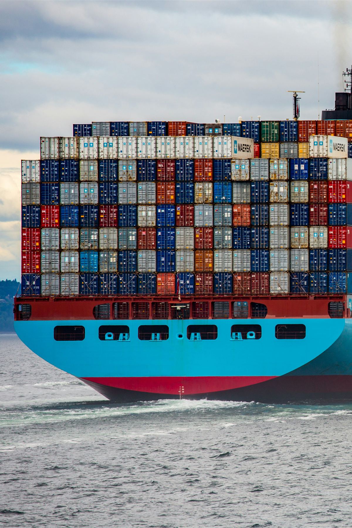 The stern of a large container ship at sea, loaded with stacked containers.